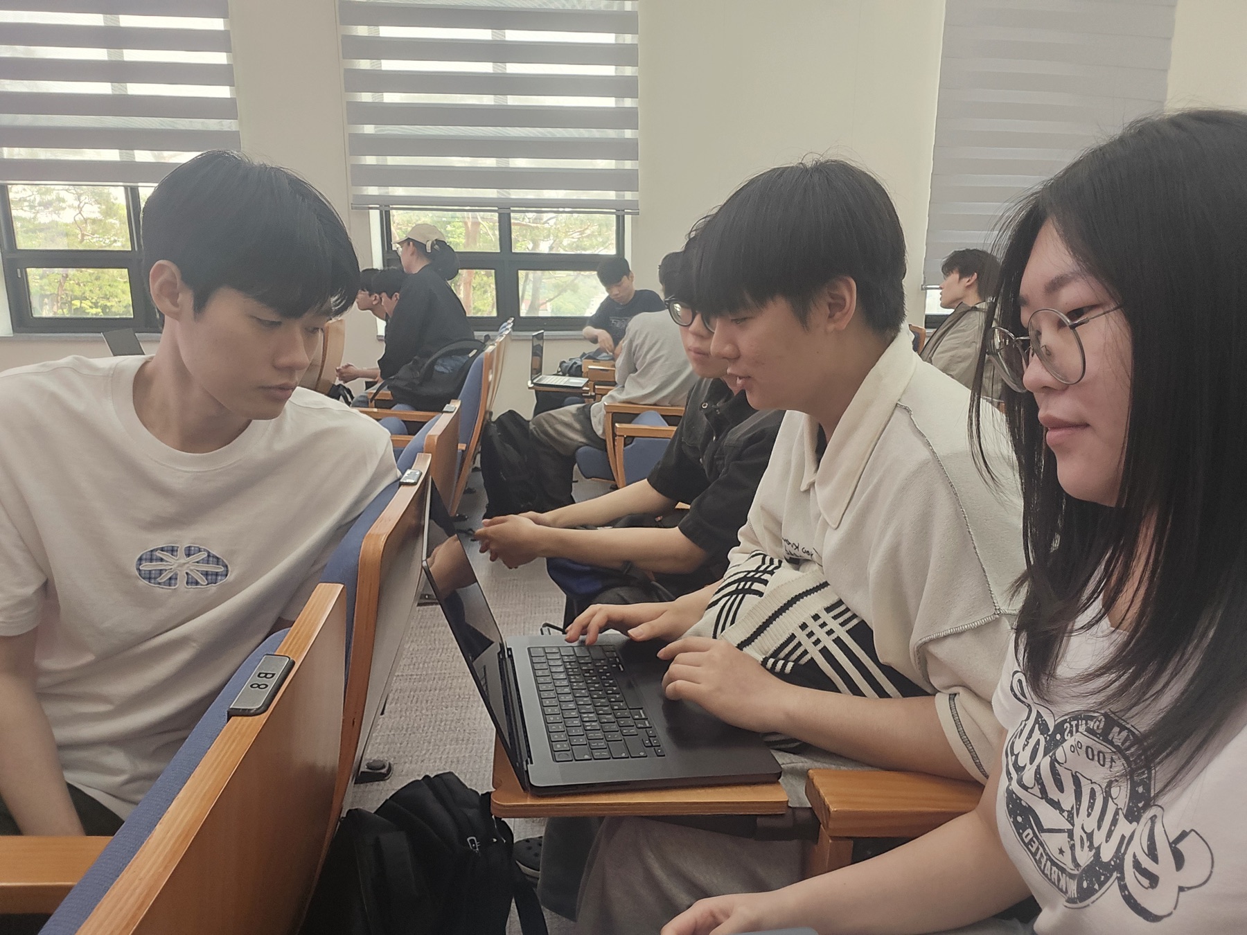 강의실에서 팀원이 함께 노트북을 보며 작업하는 모습